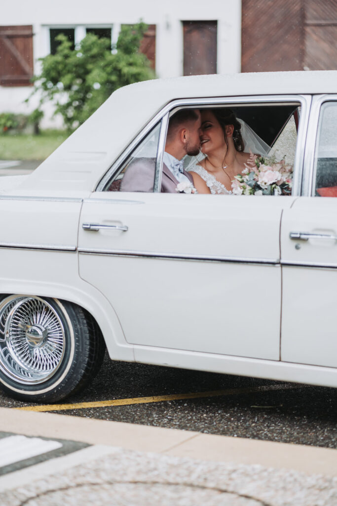 Couple de mariés qui s'embrassent discrètement dans une voiture ancienne